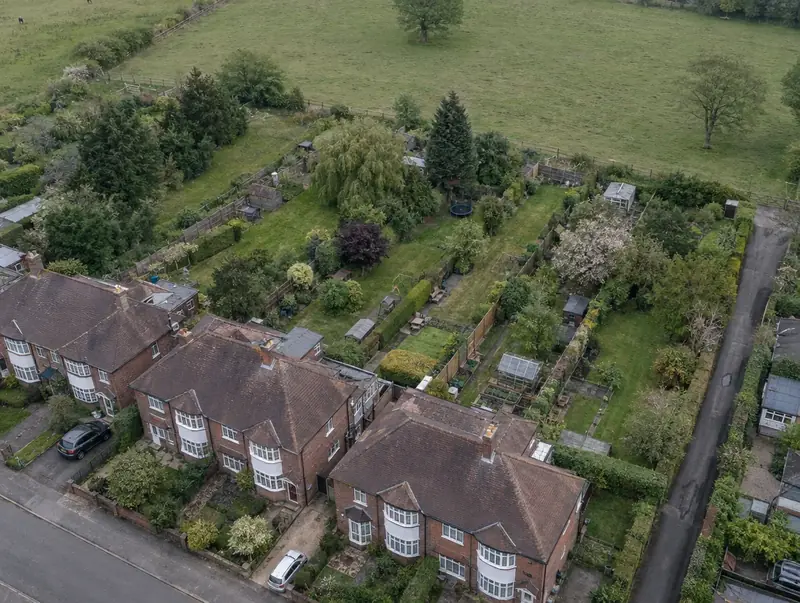 Aerial view of long rear gardens behind 1930s semi-detached houses backing onto a paddock